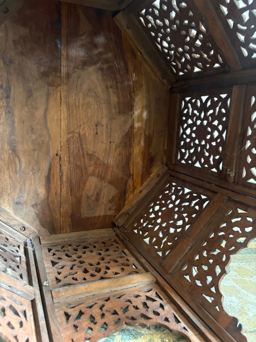 An octagonal dark teak side table featuring intricate openwork floral carving and arched fretwork base panels. View X