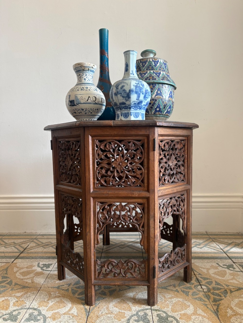 An octagonal dark teak side table featuring intricate openwork floral carving and arched fretwork base panels. View XII