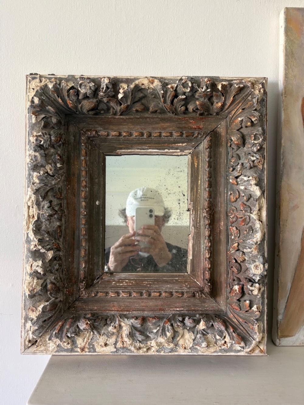 A small rectangular dark wood frame with heavily textured gesso carving enclosing a foxed mirror plate. View II