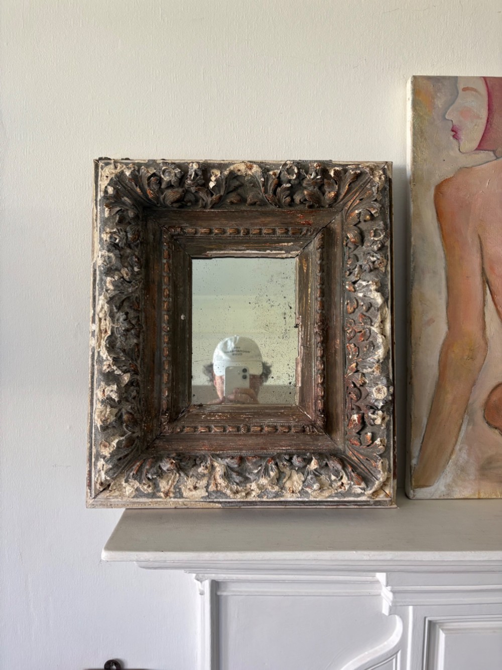 A small rectangular dark wood frame with heavily textured gesso carving enclosing a foxed mirror plate. View III