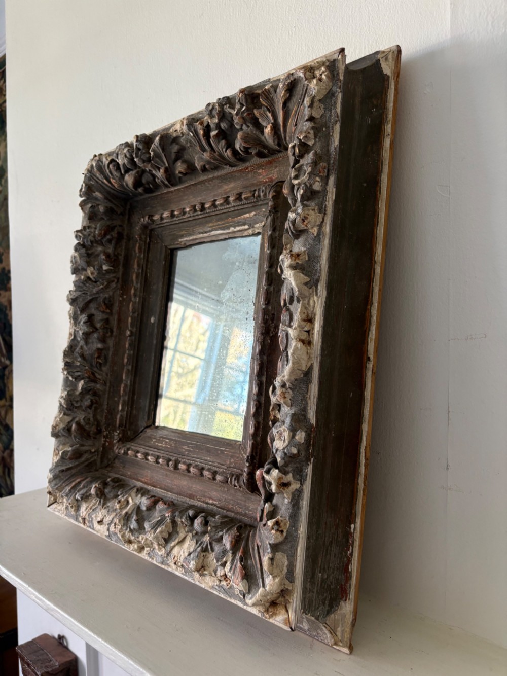 A small rectangular dark wood frame with heavily textured gesso carving enclosing a foxed mirror plate. View VI