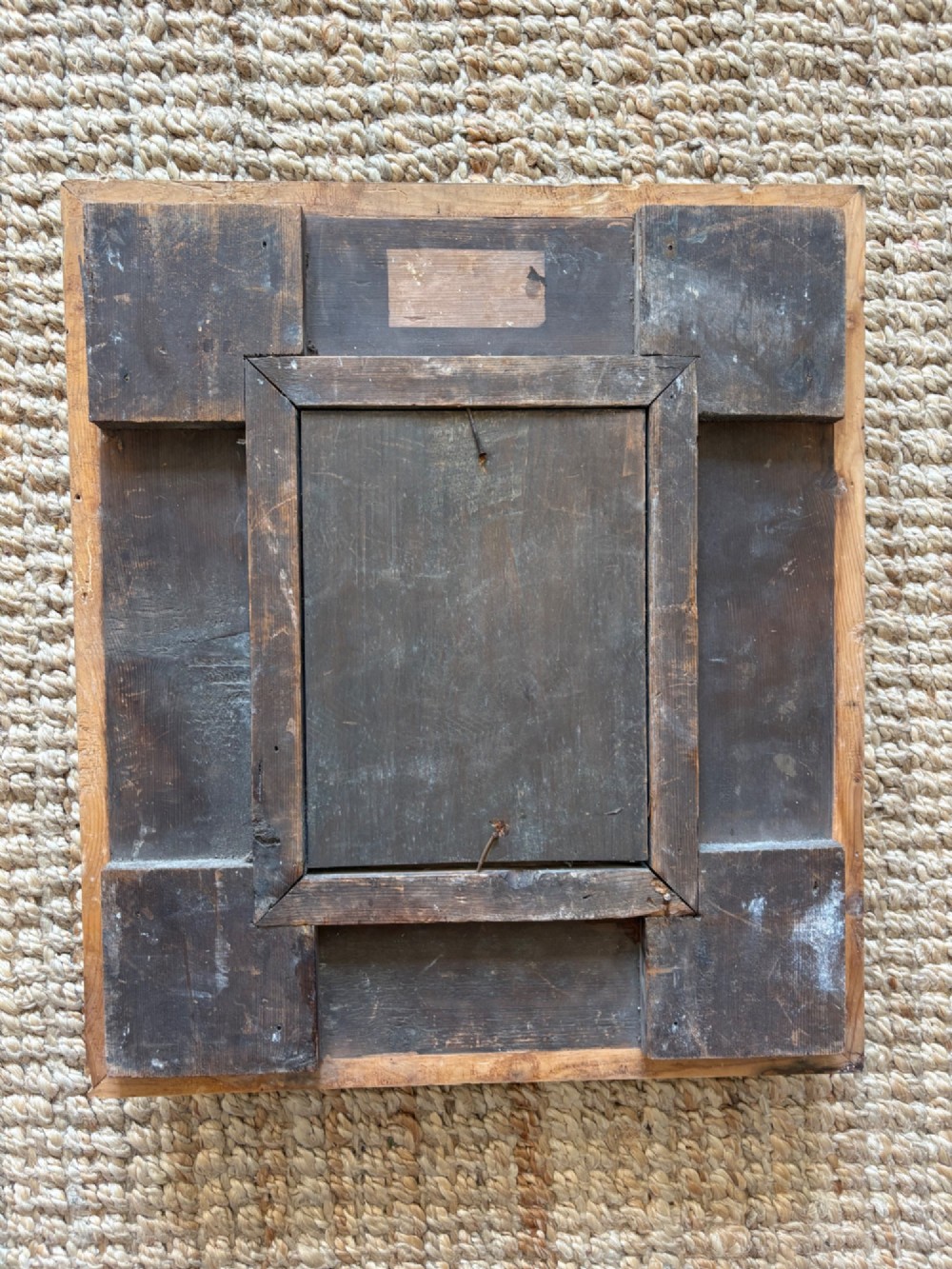 A small rectangular dark wood frame with heavily textured gesso carving enclosing a foxed mirror plate. View VII