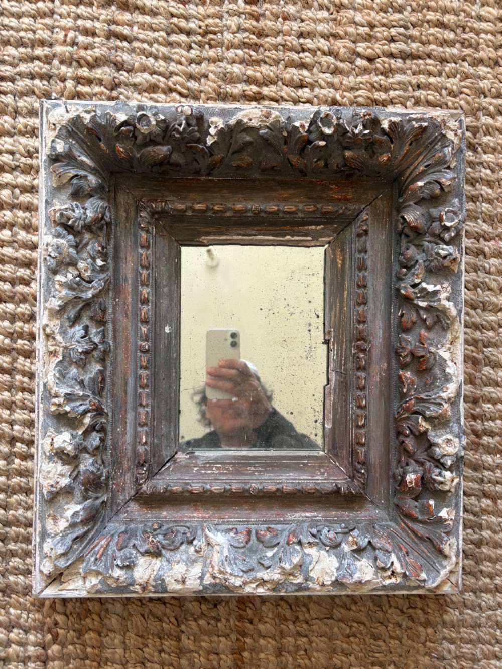 A small rectangular dark wood frame with heavily textured gesso carving enclosing a foxed mirror plate. View VIII