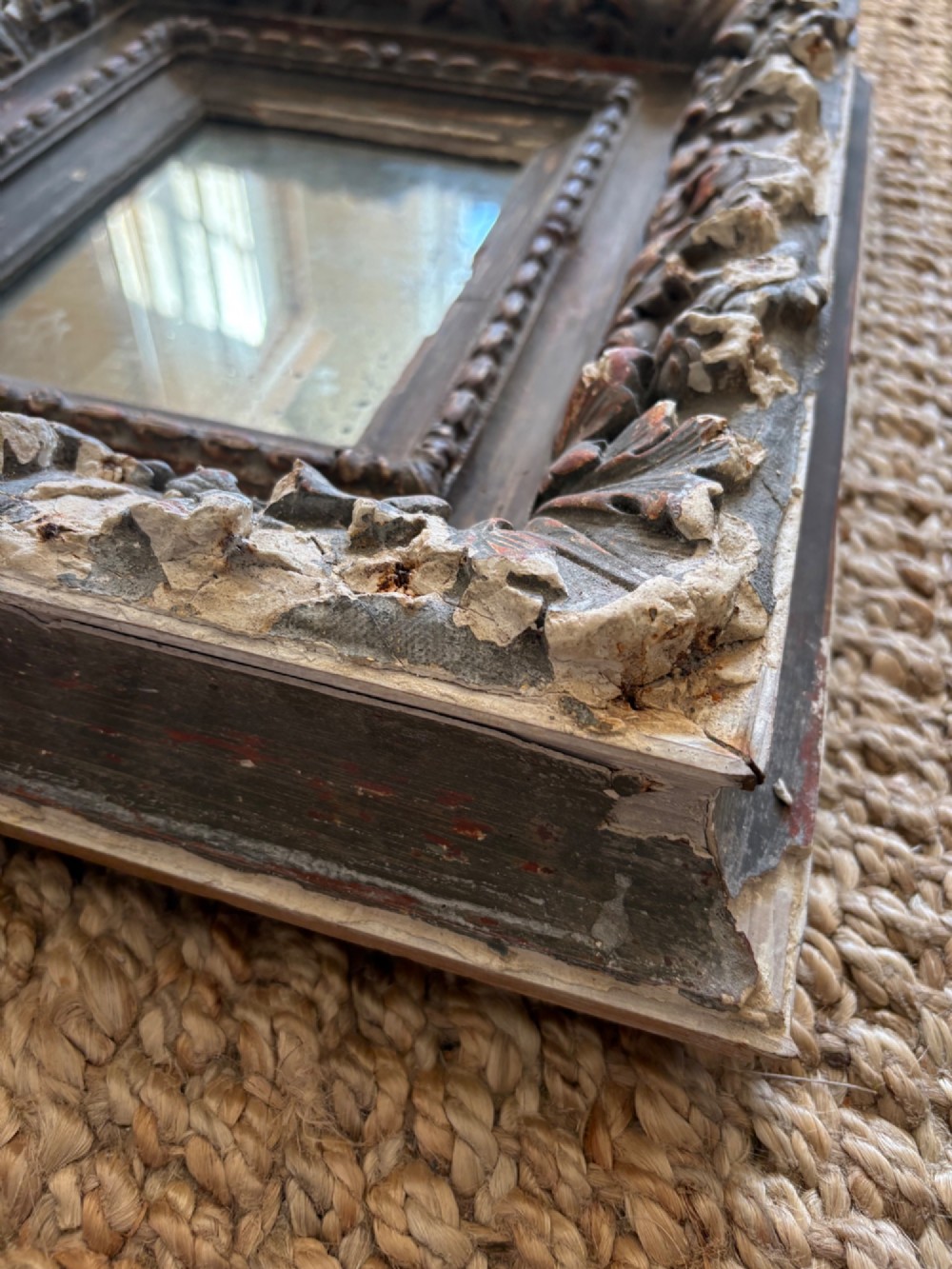 A small rectangular dark wood frame with heavily textured gesso carving enclosing a foxed mirror plate. View IX