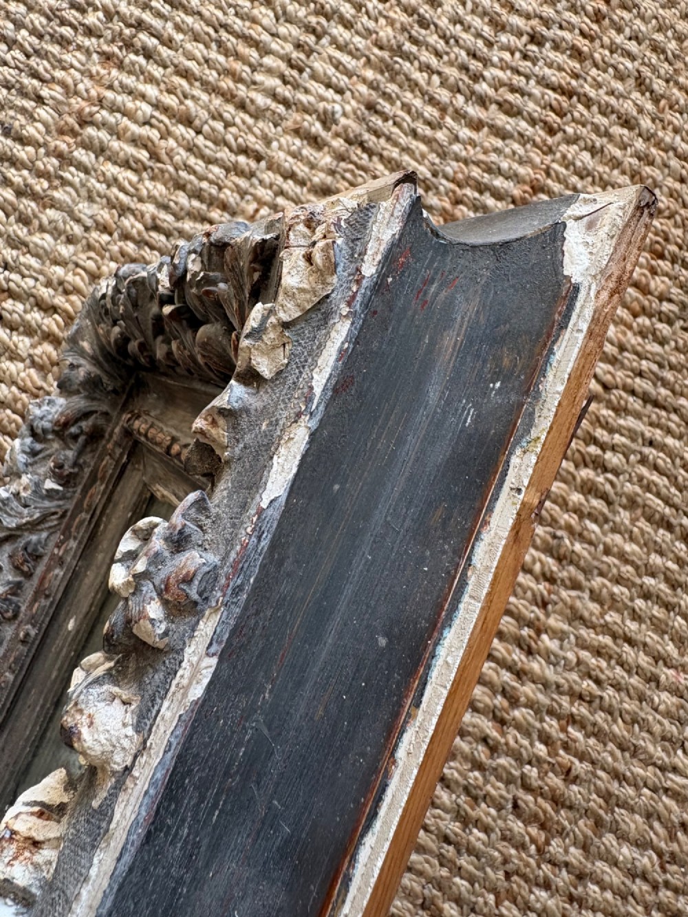 A small rectangular dark wood frame with heavily textured gesso carving enclosing a foxed mirror plate. View X