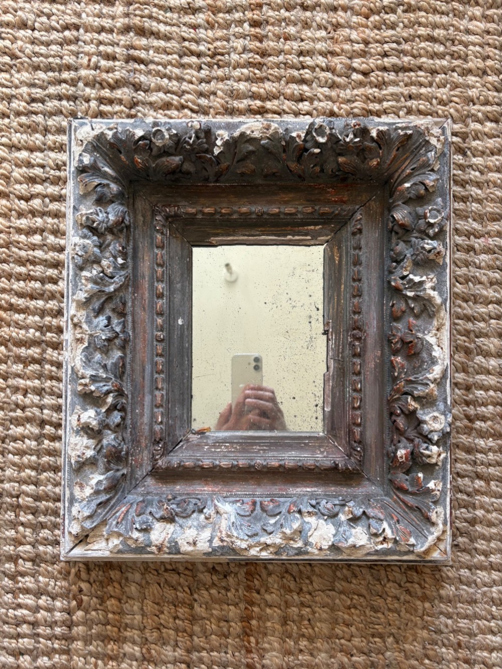 A small rectangular dark wood frame with heavily textured gesso carving enclosing a foxed mirror plate. View XI