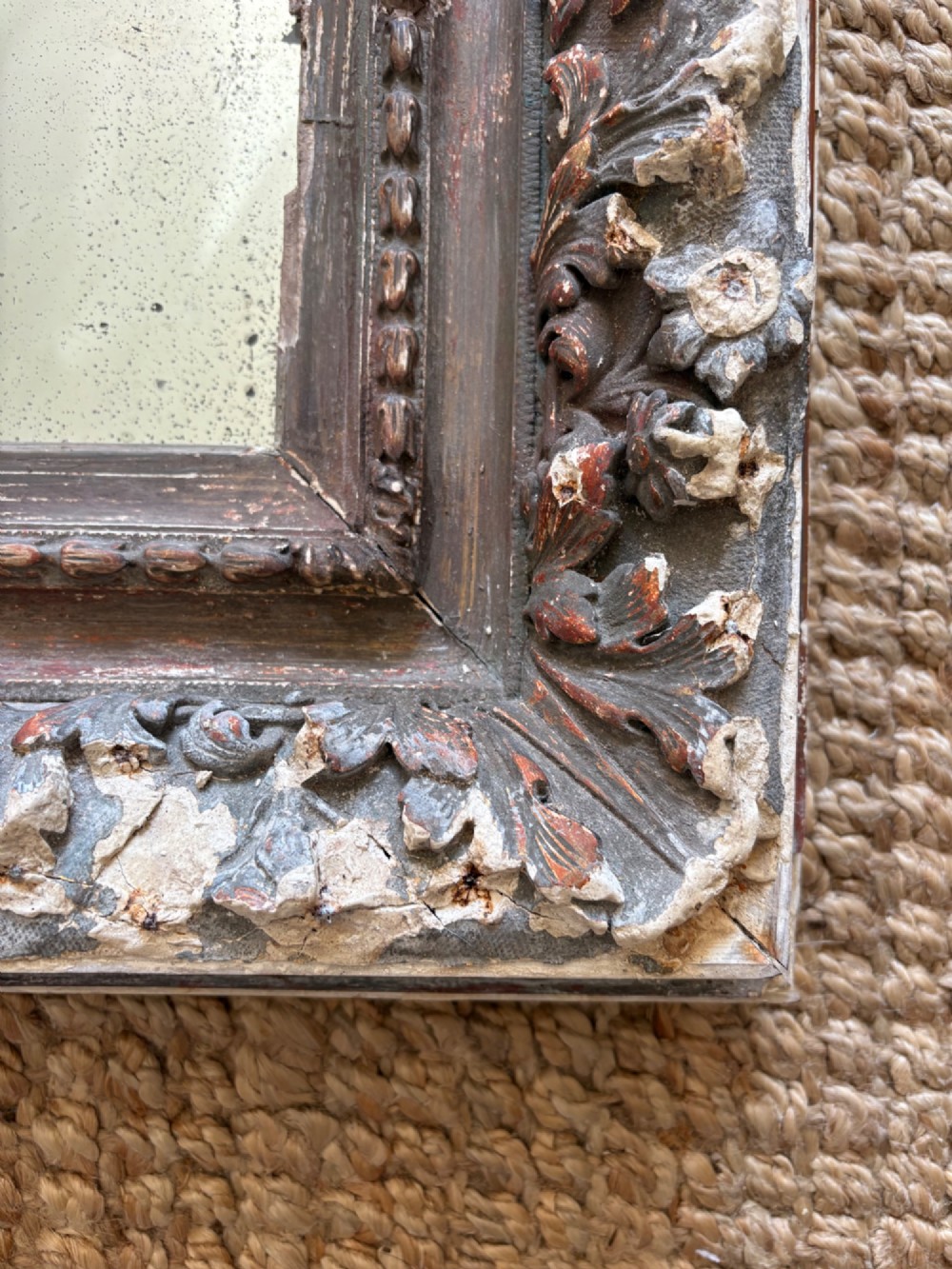 A small rectangular dark wood frame with heavily textured gesso carving enclosing a foxed mirror plate. View XII