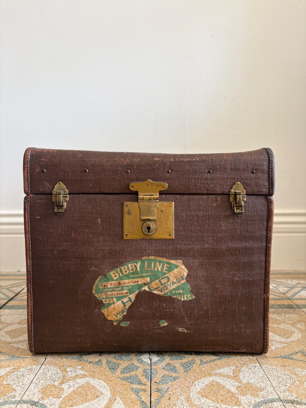 An Edwardian brown canvas and leather hat box trunk featuring brass latches, stitched leather trim, and an ocean liner travel label on the front. View III