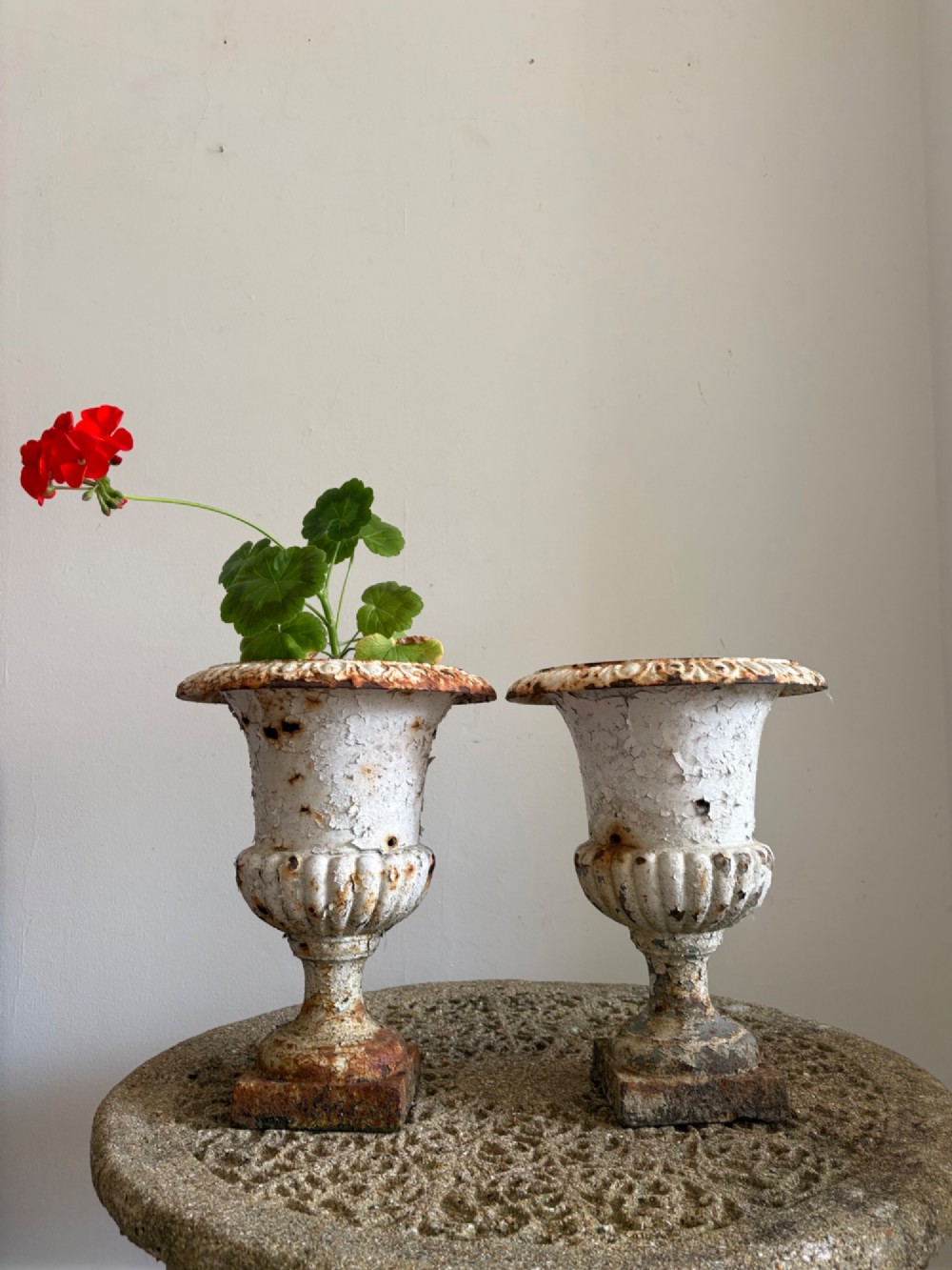 A pair of 19th-century classical cast iron garden urns featuring distressed flaking white paint, fluted bowls, and square bases.