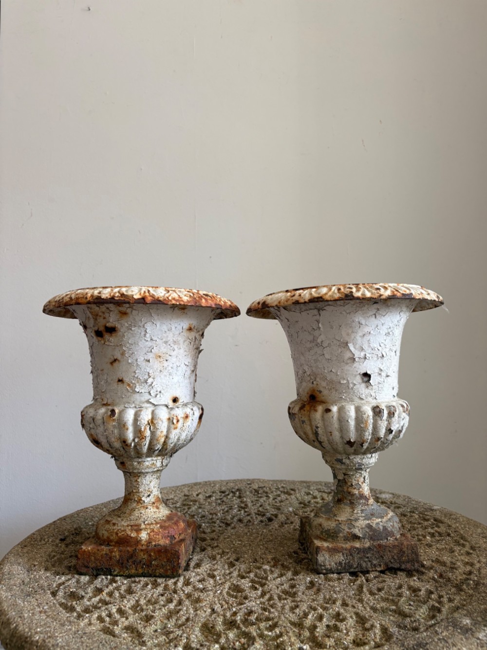 A pair of 19th-century classical cast iron garden urns featuring distressed flaking white paint, fluted bowls, and square bases. View II
