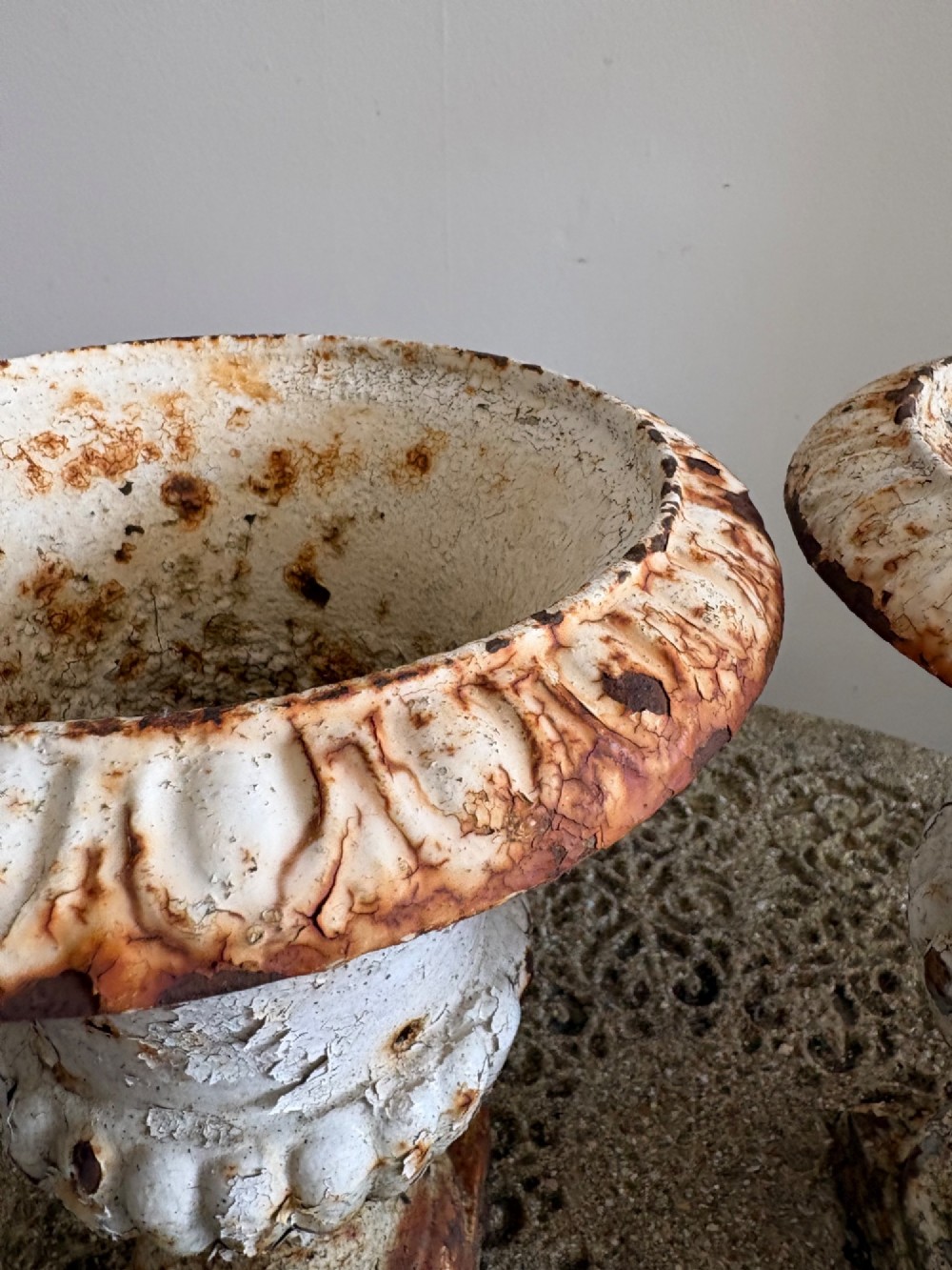 A pair of 19th-century classical cast iron garden urns featuring distressed flaking white paint, fluted bowls, and square bases. View V