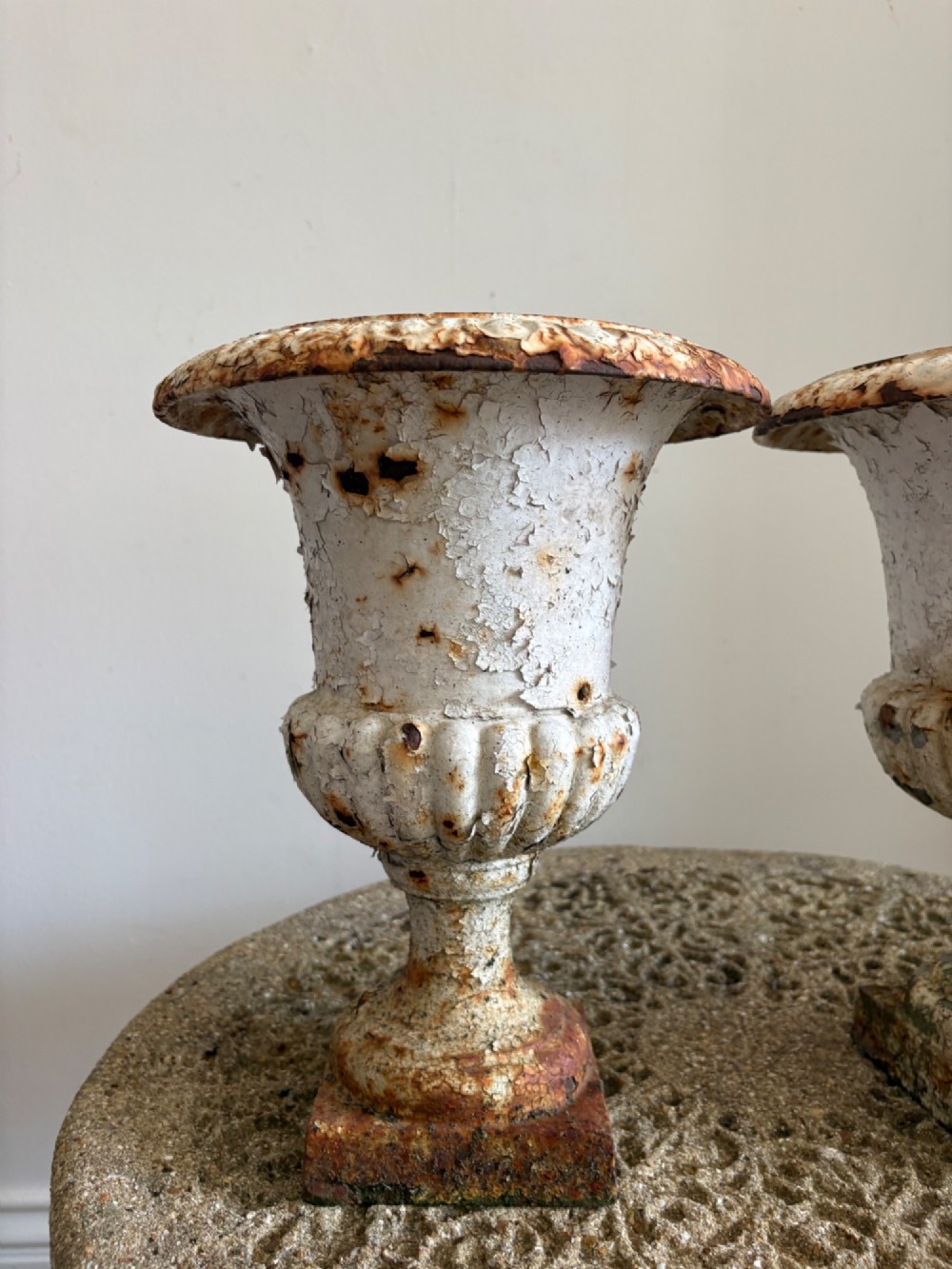 A pair of 19th-century classical cast iron garden urns featuring distressed flaking white paint, fluted bowls, and square bases. View VI