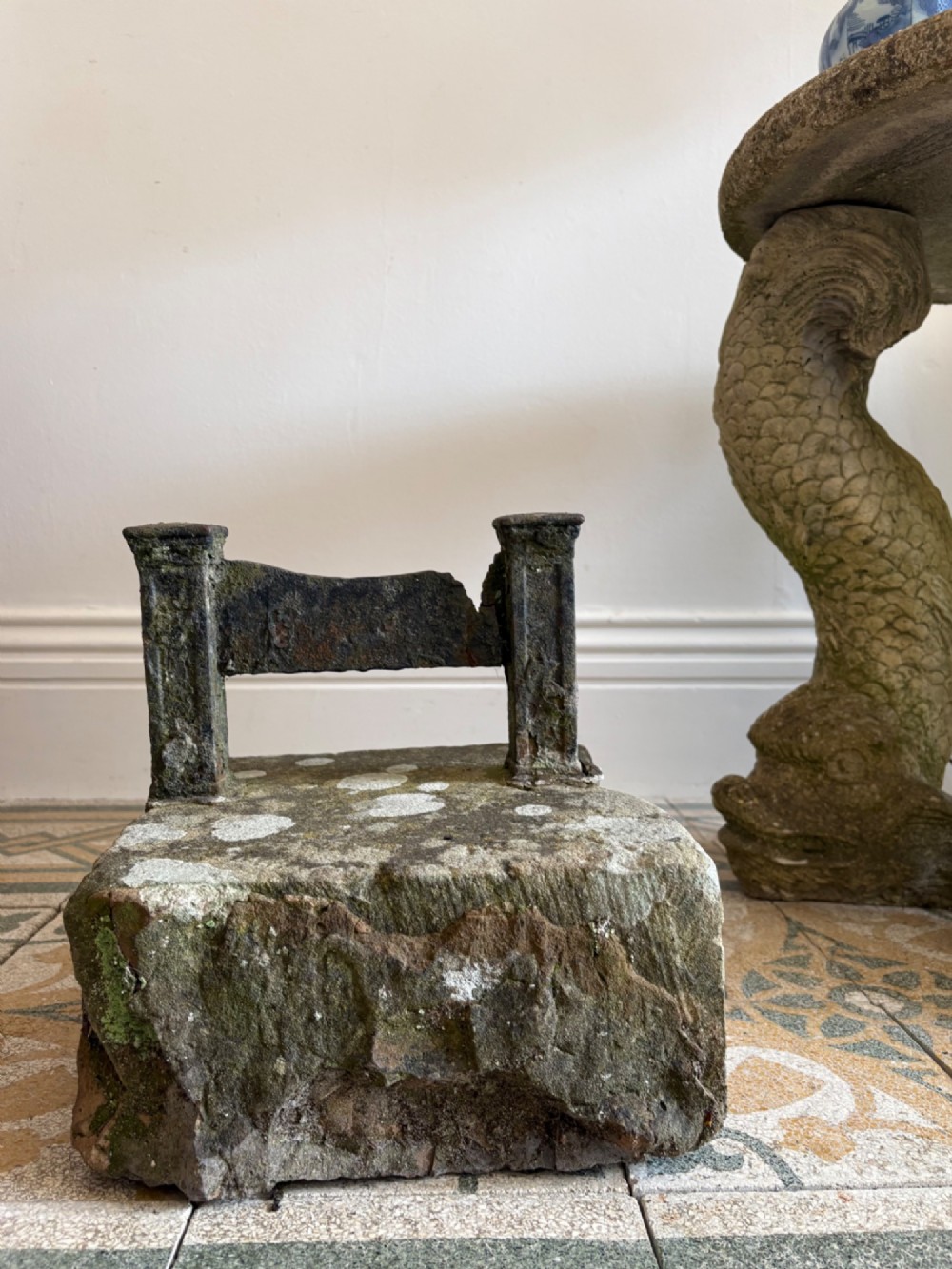 A 19th-century cast iron boot scraper with a central scraping blade set between two vertical pillars, mounted into a heavy hand-hewn stone block.