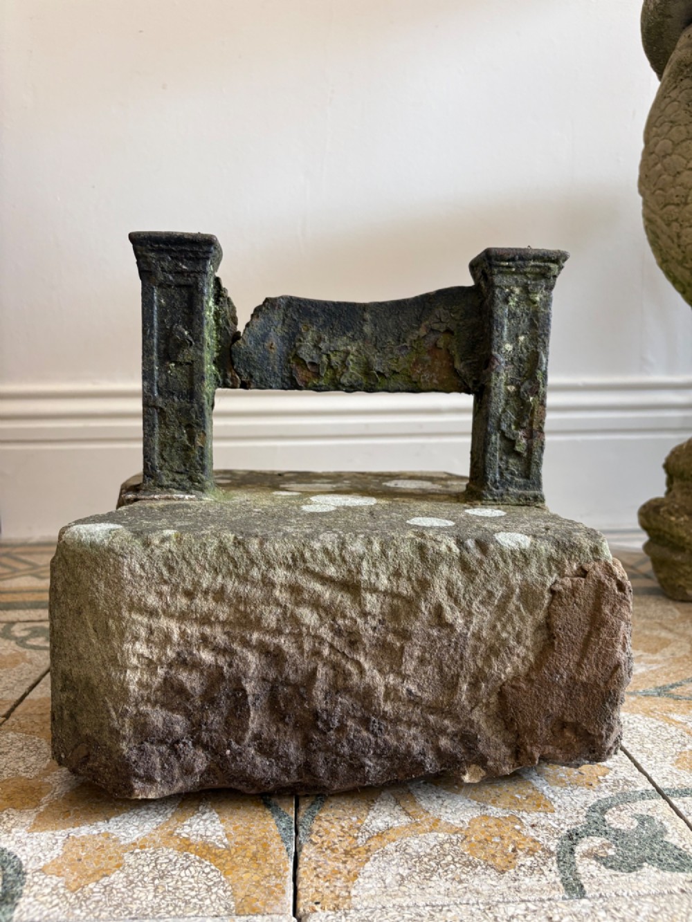 A 19th-century cast iron boot scraper with a central scraping blade set between two vertical pillars, mounted into a heavy hand-hewn stone block. View IX