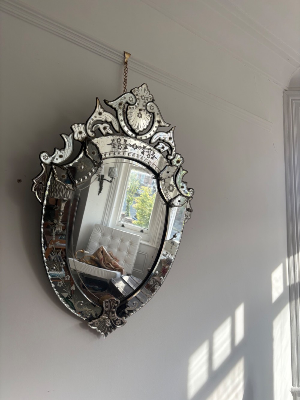 An oval Venetian wall mirror featuring an etched glass frame with floral motifs, a scrollwork crest, and a bevelled centre mirror with light foxing.