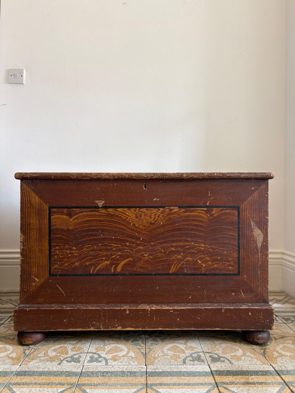 A 19th-century rectangular pine trunk featuring decorative scumble glazed painted panels, a hinged lid, and turned bun feet.