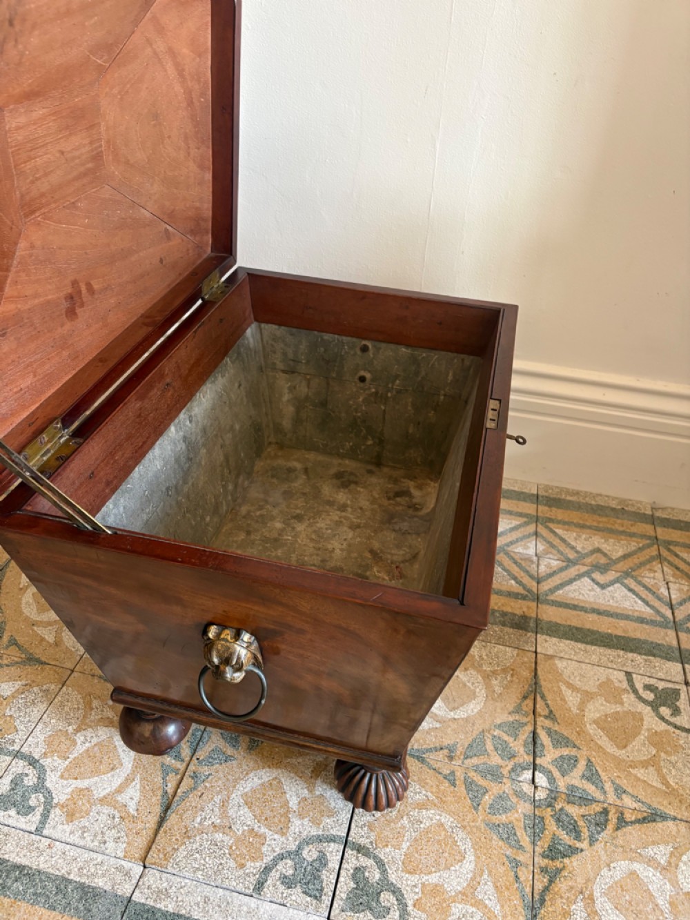 A Regency tapered mahogany sarcophagus cellarette featuring a hinged lid, keyhole with brass escutcheon, and turned gadrooned feet. View IV