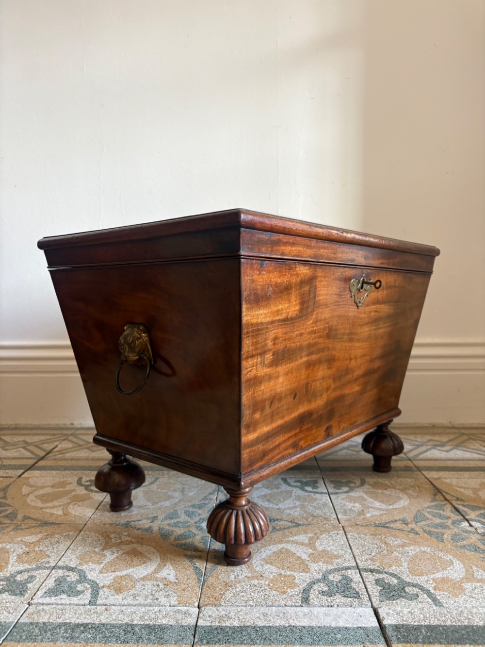 A Regency tapered mahogany sarcophagus cellarette featuring a hinged lid, keyhole with brass escutcheon, and turned gadrooned feet. View V