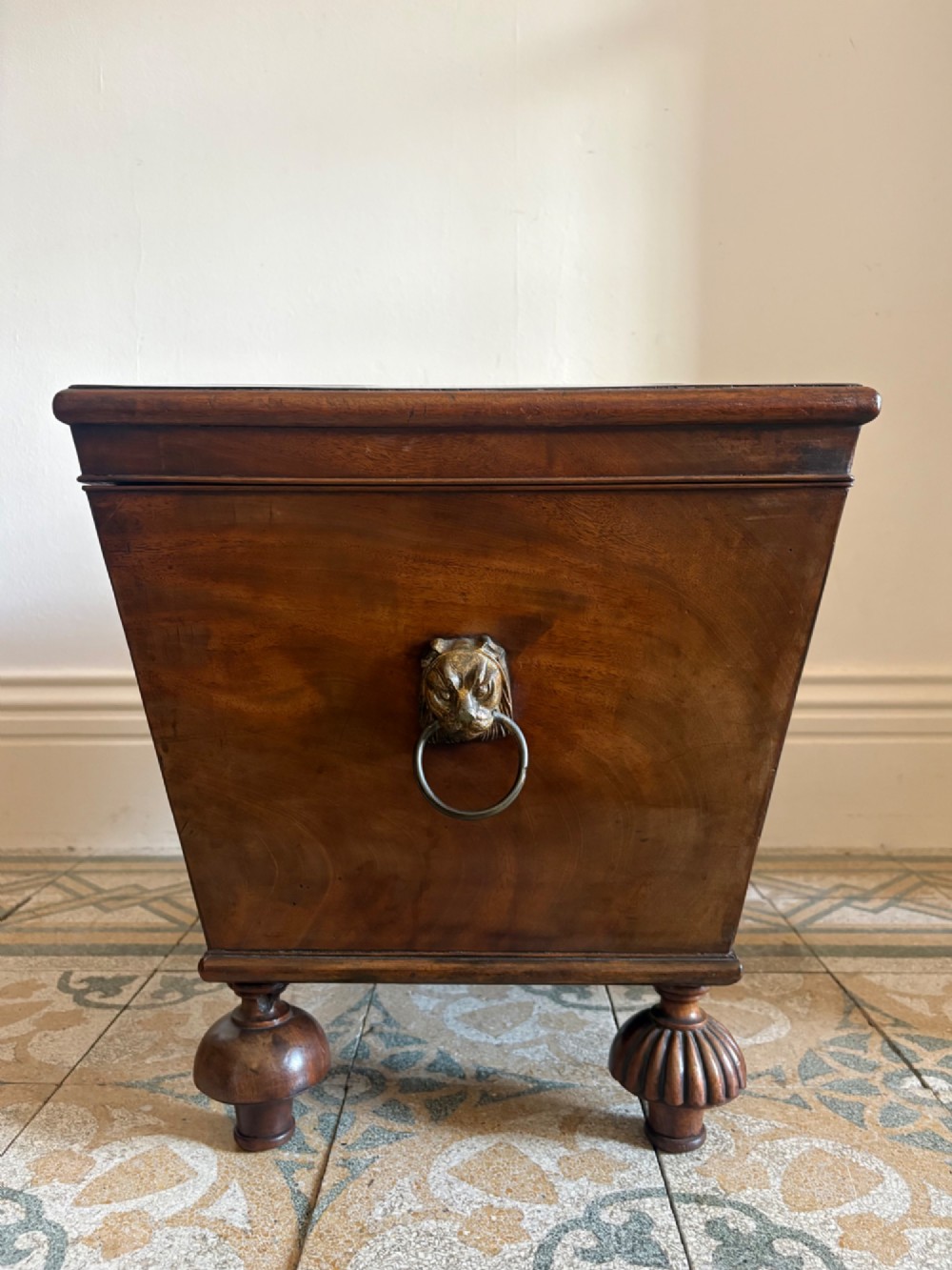 A Regency tapered mahogany sarcophagus cellarette featuring a hinged lid, keyhole with brass escutcheon, and turned gadrooned feet. View VII