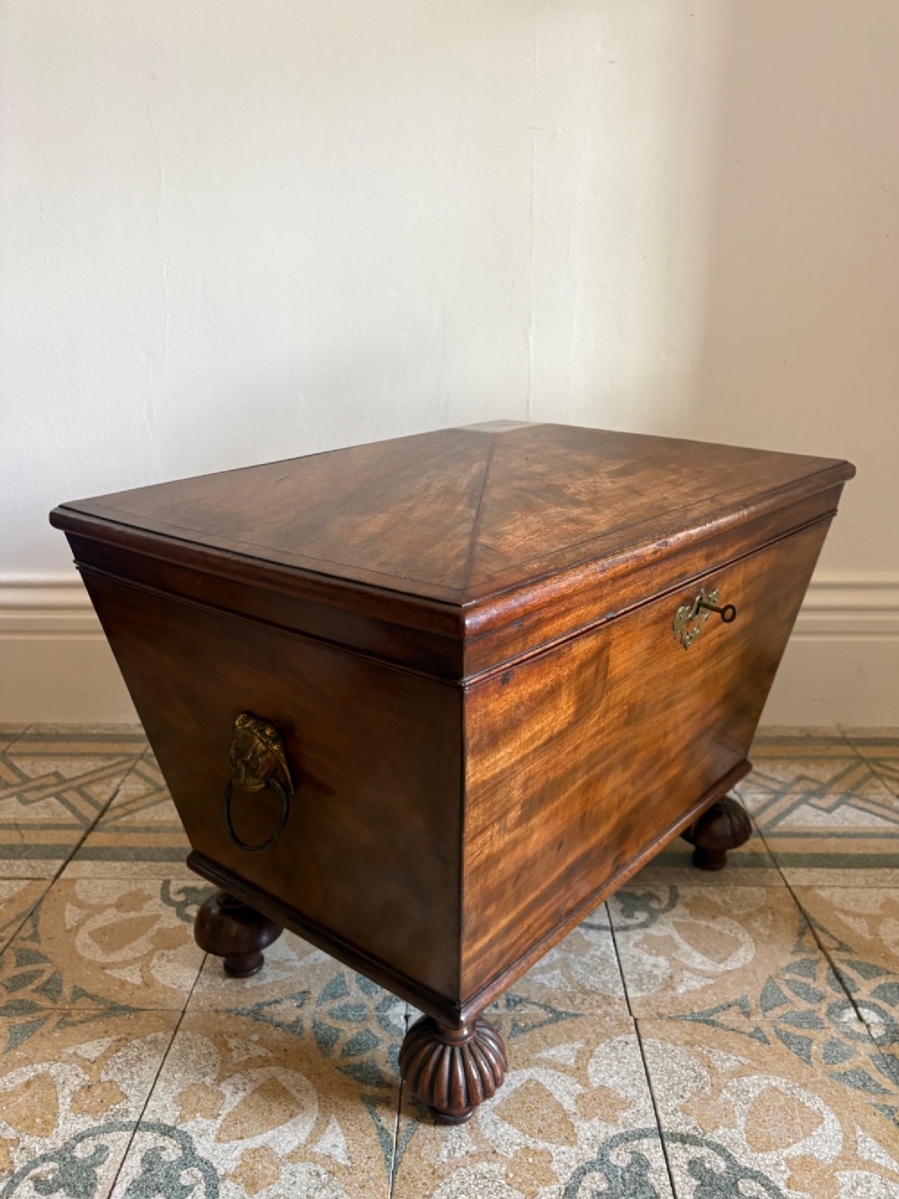 A Regency tapered mahogany sarcophagus cellarette featuring a hinged lid, keyhole with brass escutcheon, and turned gadrooned feet. View XI