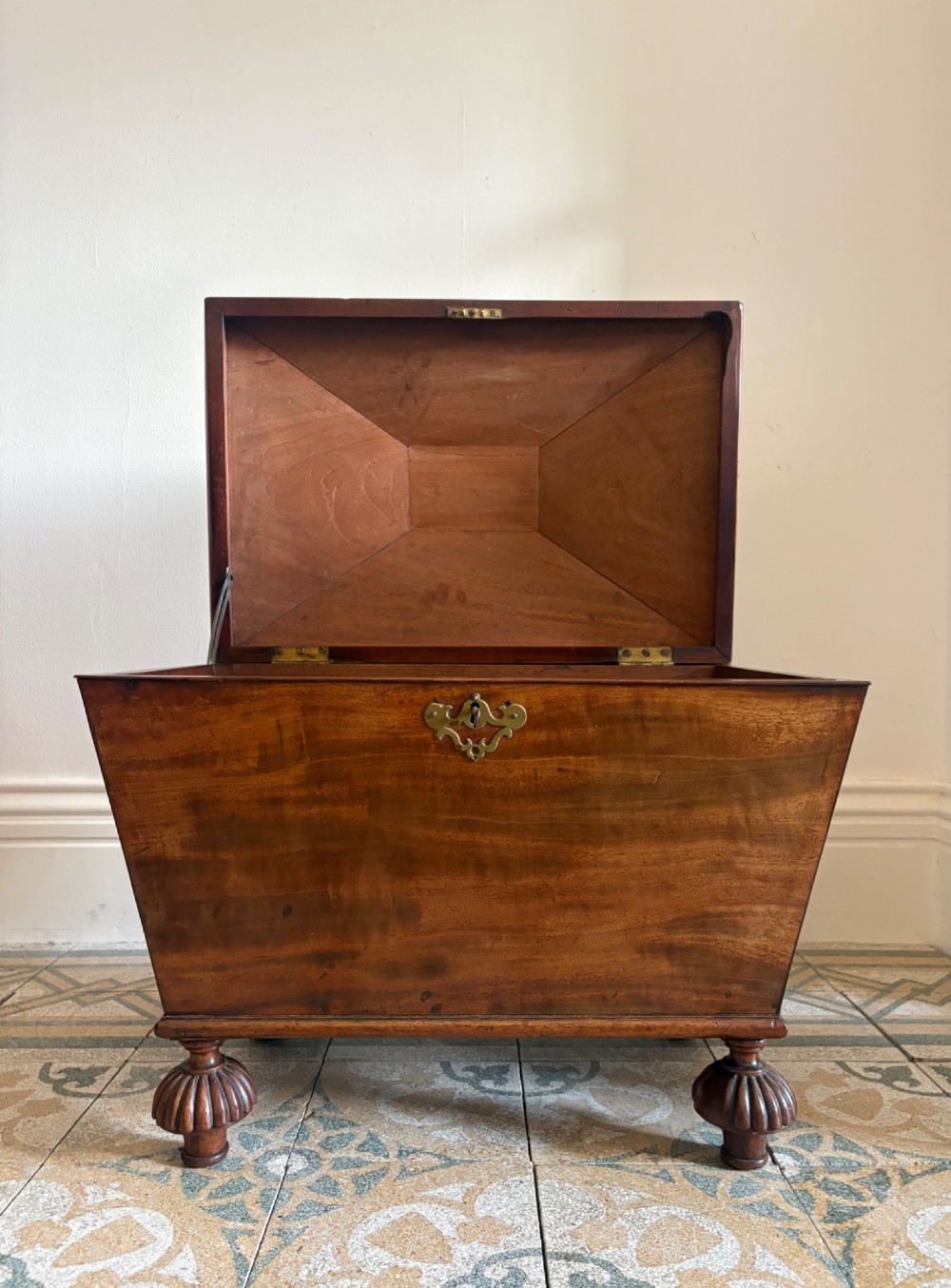 A Regency tapered mahogany sarcophagus cellarette featuring a hinged lid, keyhole with brass escutcheon, and turned gadrooned feet. View XIII