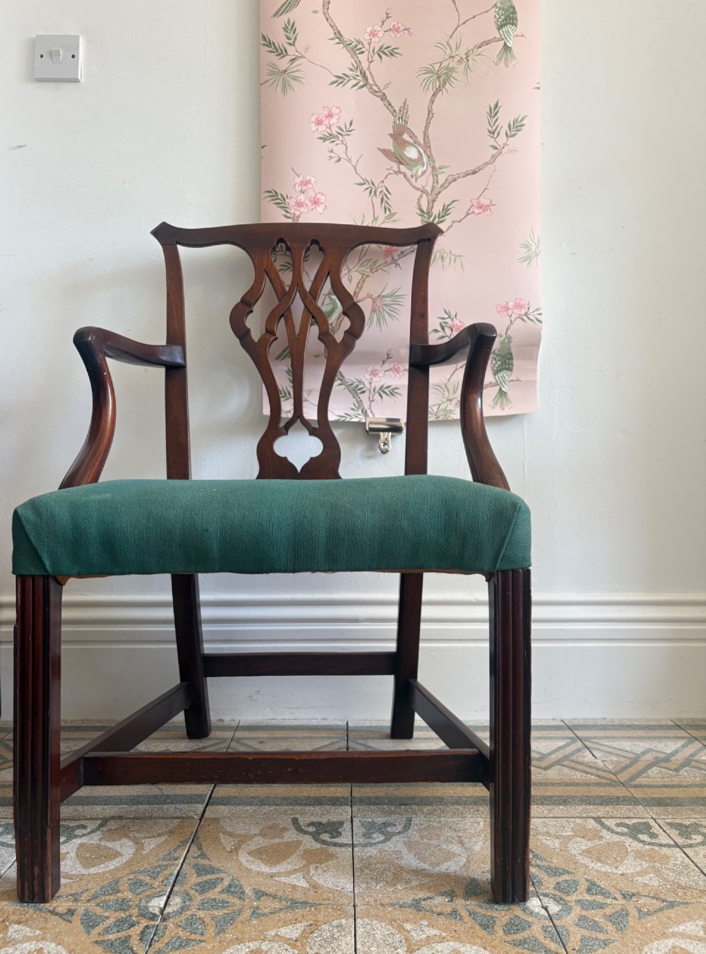 A George III mahogany elbow chair featuring a carved pierced splat back, swept armrests, and a green upholstered seat. View II