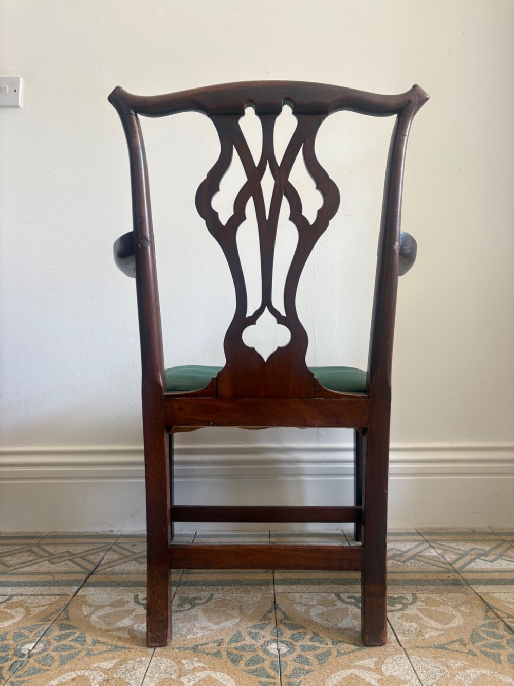 A George III mahogany elbow chair featuring a carved pierced splat back, swept armrests, and a green upholstered seat. View III