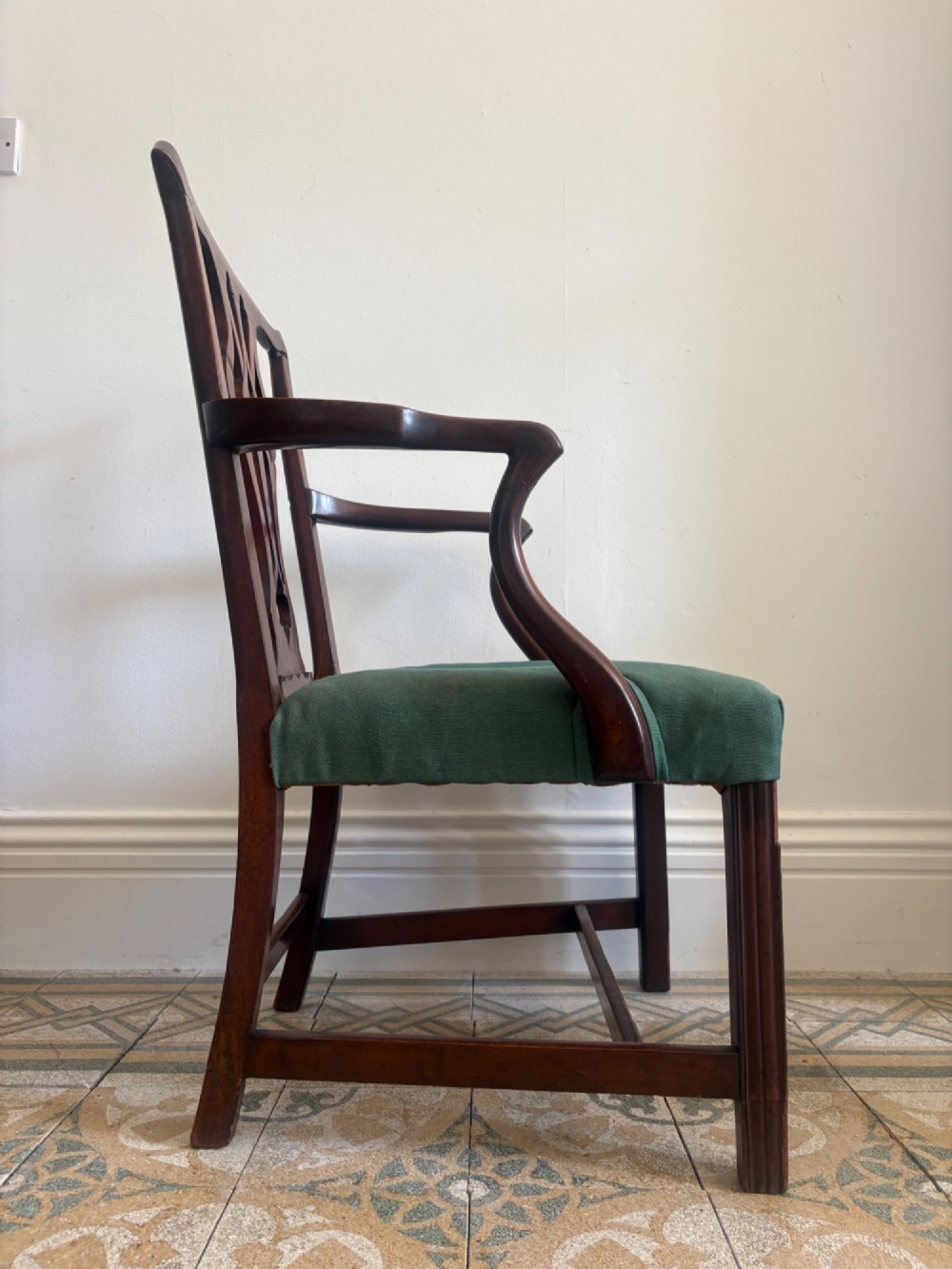 A George III mahogany elbow chair featuring a carved pierced splat back, swept armrests, and a green upholstered seat. View IV