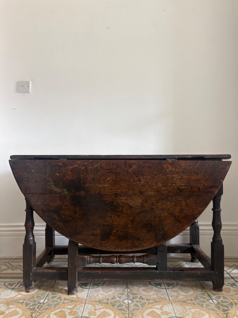 A dark oak gateleg table with a drop-leaf plank top and turned baluster legs joined by low stretchers.