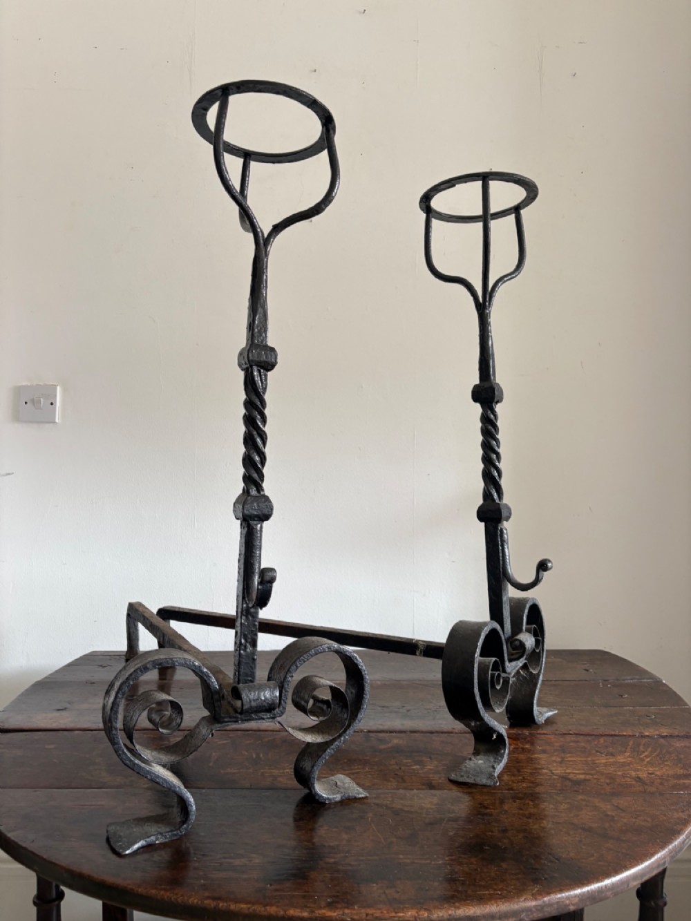 A pair of tall 19th-century black wrought iron fire dogs featuring hand-twisted shafts, scrollwork feet, and circular top ring terminals.