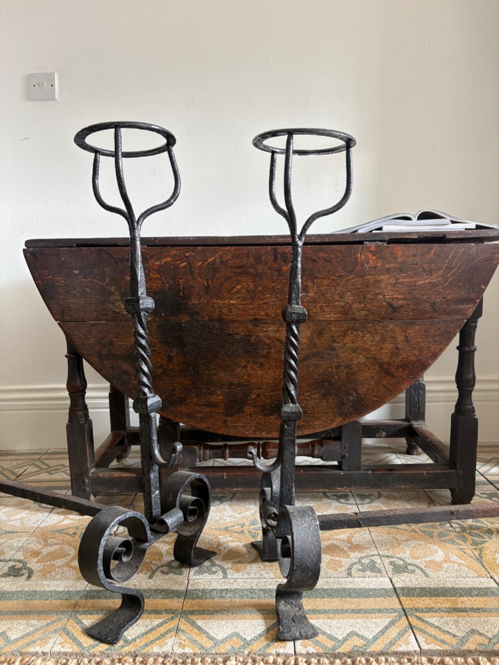 A pair of tall 19th-century black wrought iron fire dogs featuring hand-twisted shafts, scrollwork feet, and circular top ring terminals. View II