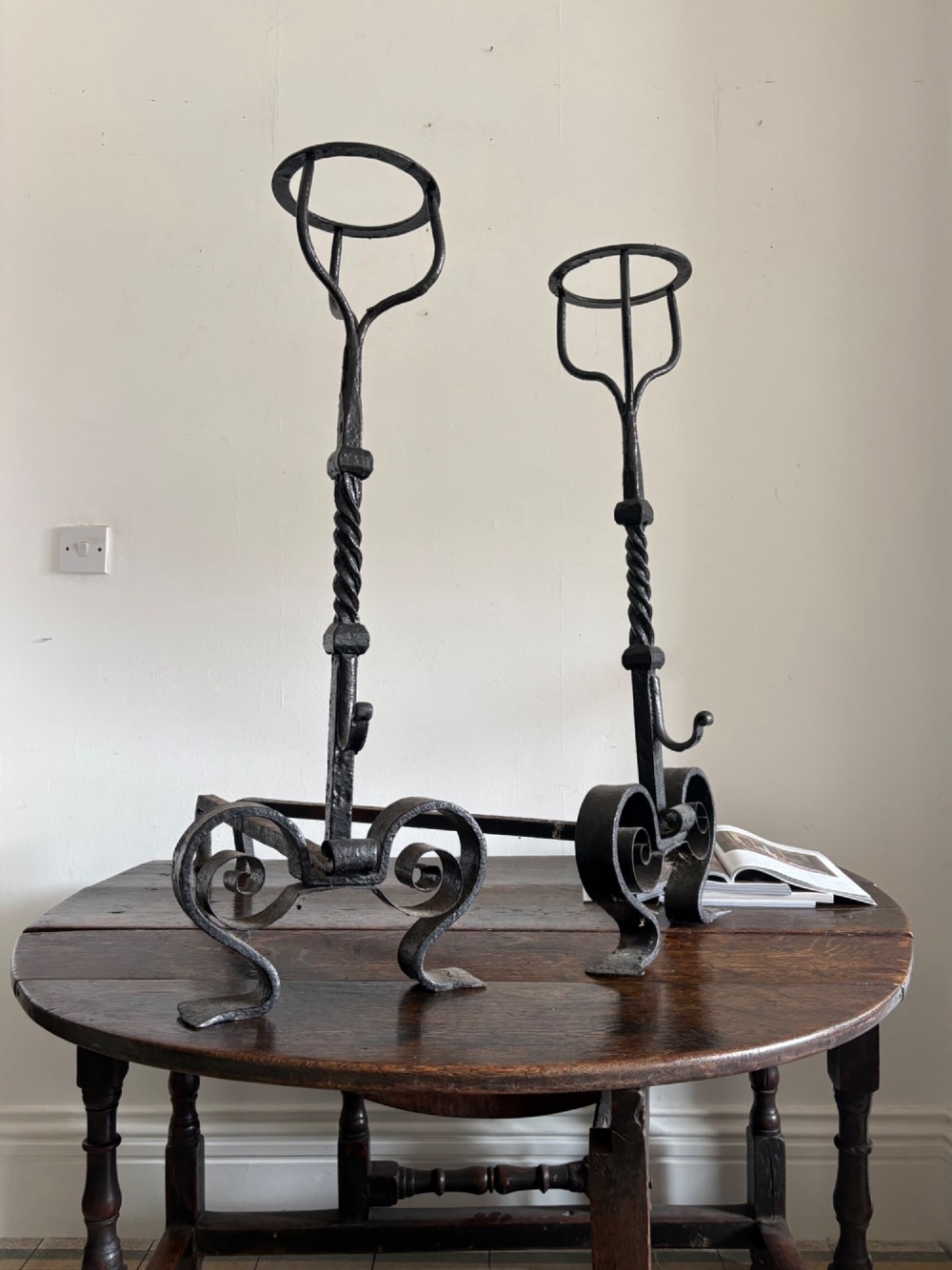 A pair of tall 19th-century black wrought iron fire dogs featuring hand-twisted shafts, scrollwork feet, and circular top ring terminals. View IV