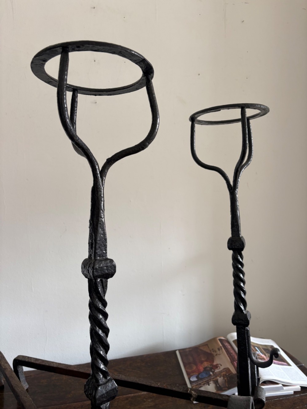 A pair of tall 19th-century black wrought iron fire dogs featuring hand-twisted shafts, scrollwork feet, and circular top ring terminals. View IX