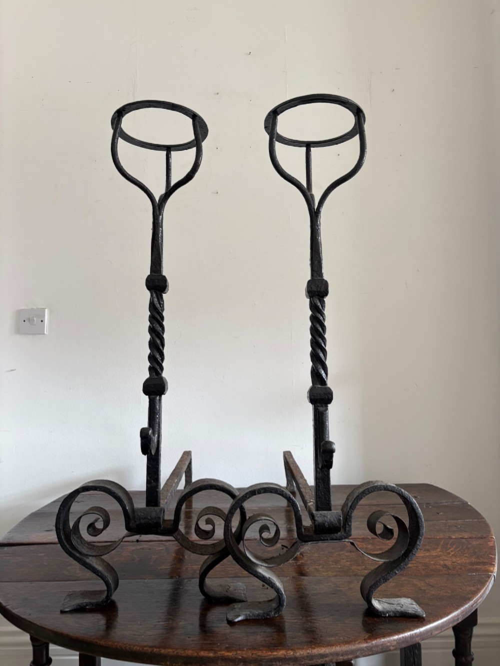 A pair of tall 19th-century black wrought iron fire dogs featuring hand-twisted shafts, scrollwork feet, and circular top ring terminals. View X