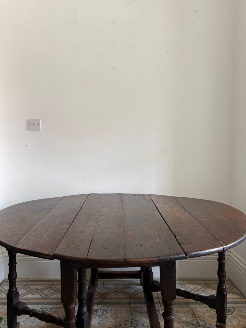 A dark oak gateleg table with a drop-leaf plank top and turned baluster legs joined by low stretchers. View XII