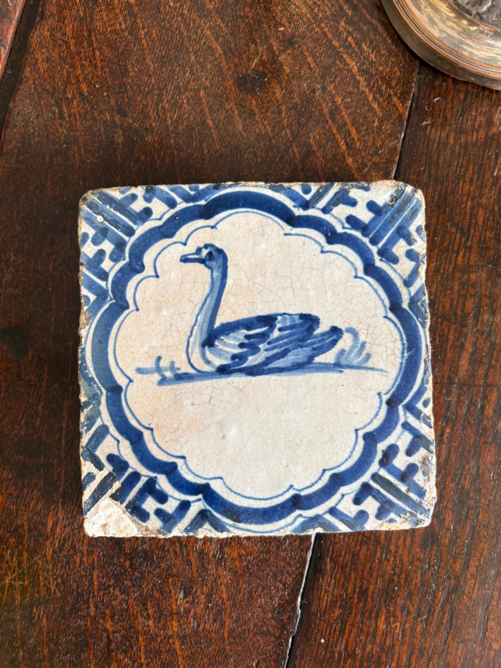 A square 17th-century tin-glazed earthenware tile featuring a hand-painted cobalt blue swan motif inside a scalloped border with geometric corner details.