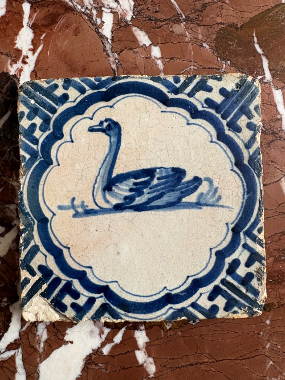 A square 17th-century tin-glazed earthenware tile featuring a hand-painted cobalt blue swan motif inside a scalloped border with geometric corner details. View II