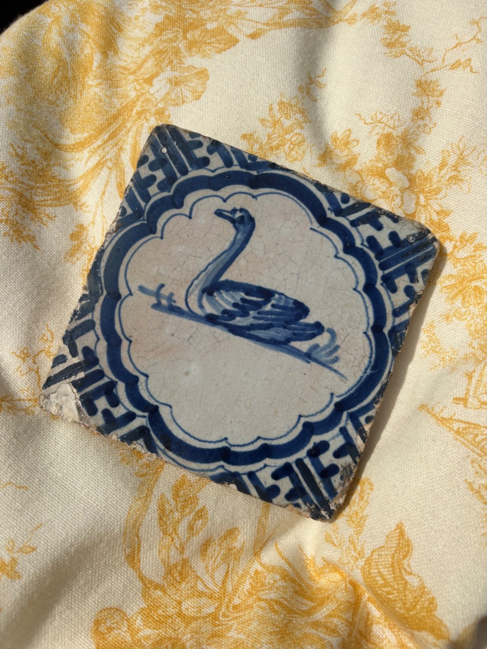 A square 17th-century tin-glazed earthenware tile featuring a hand-painted cobalt blue swan motif inside a scalloped border with geometric corner details. View XIV