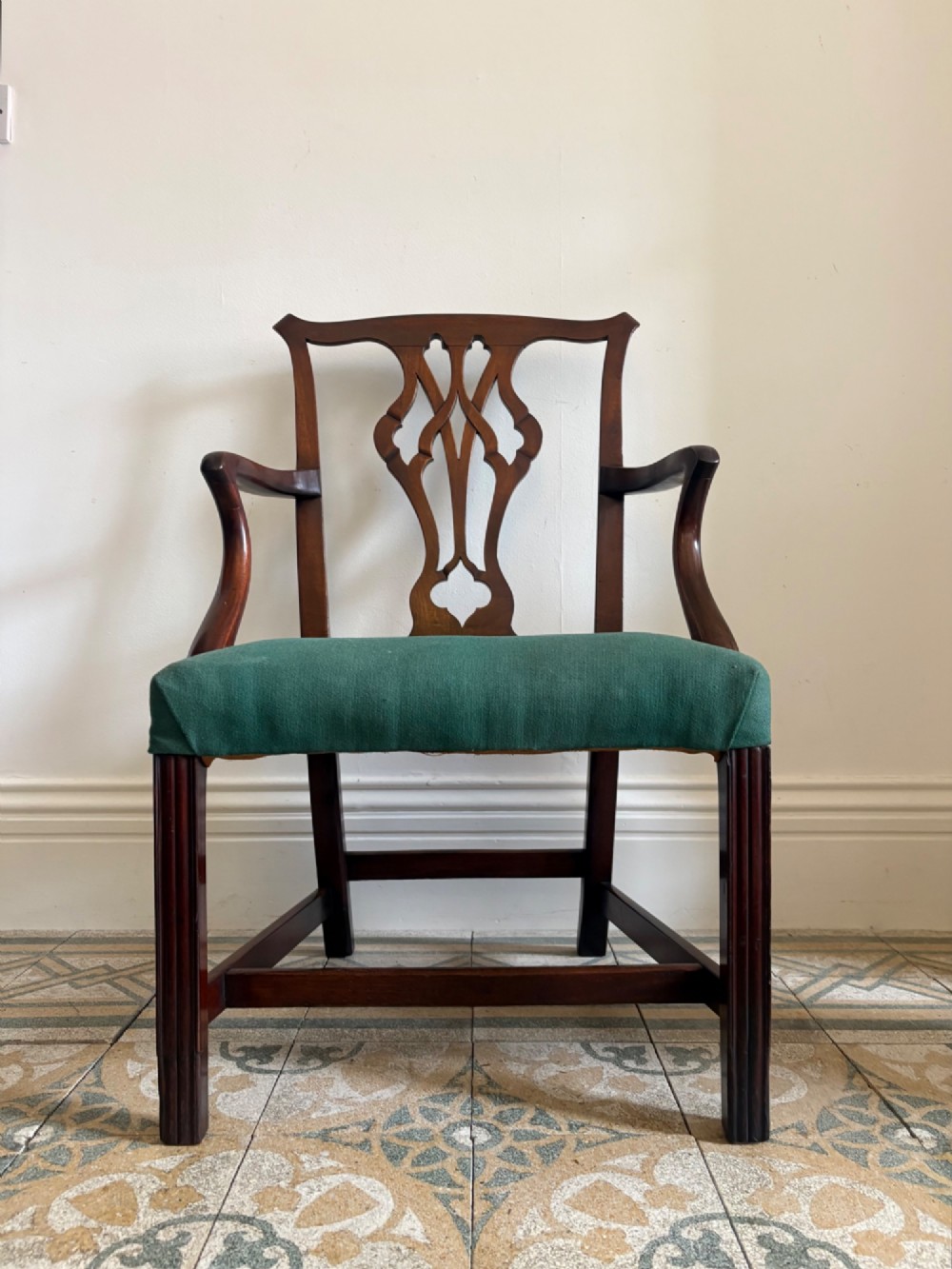 A George III mahogany elbow chair featuring a carved pierced splat back, swept armrests, and a green upholstered seat.
