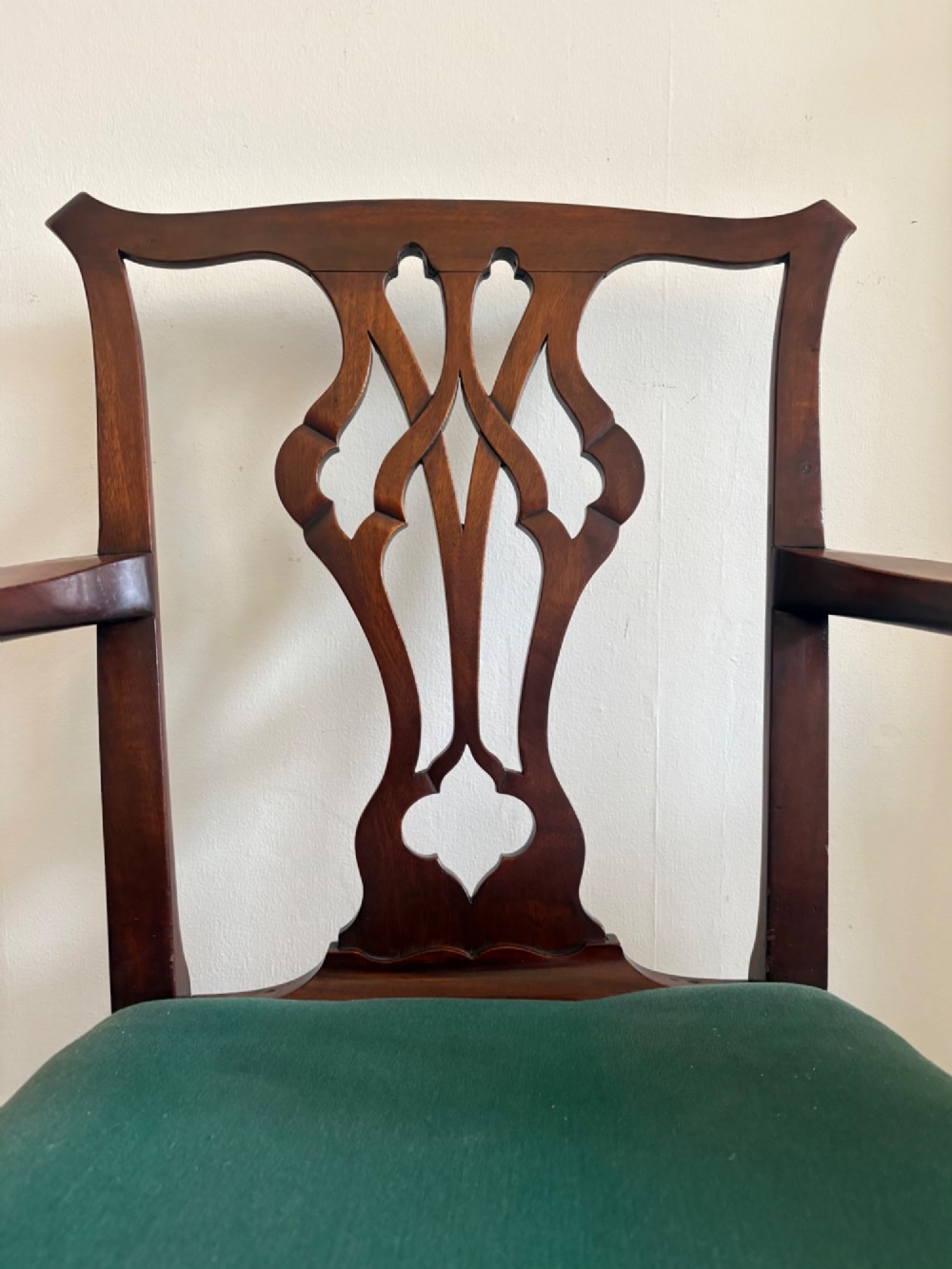 A George III mahogany elbow chair featuring a carved pierced splat back, swept armrests, and a green upholstered seat. View X