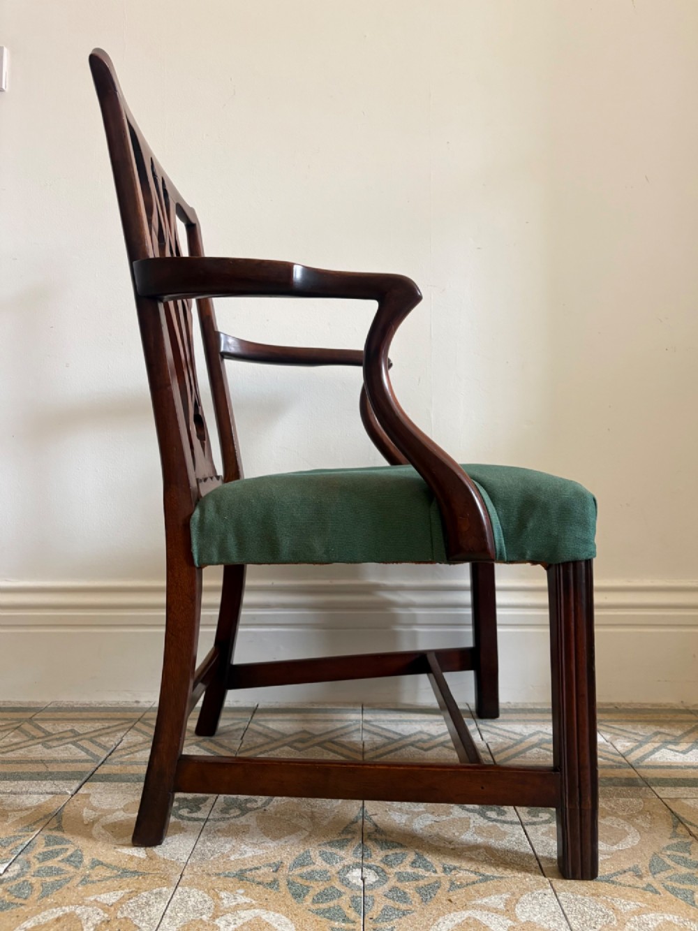 A George III mahogany elbow chair featuring a carved pierced splat back, swept armrests, and a green upholstered seat. View XI