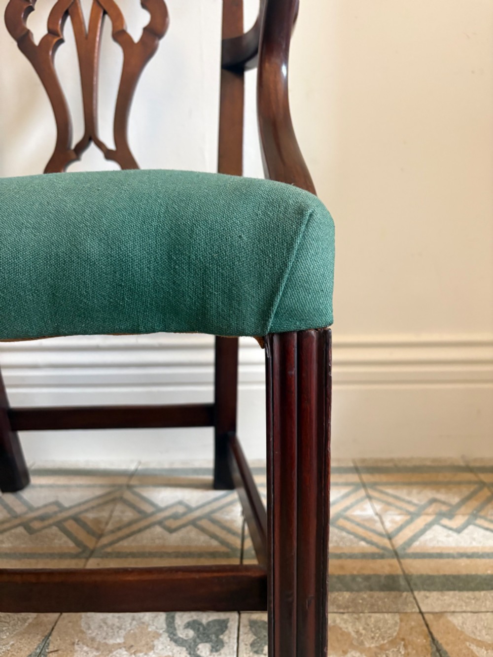A George III mahogany elbow chair featuring a carved pierced splat back, swept armrests, and a green upholstered seat. View XII