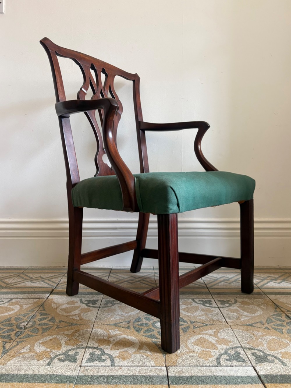 A George III mahogany elbow chair featuring a carved pierced splat back, swept armrests, and a green upholstered seat. View XIII