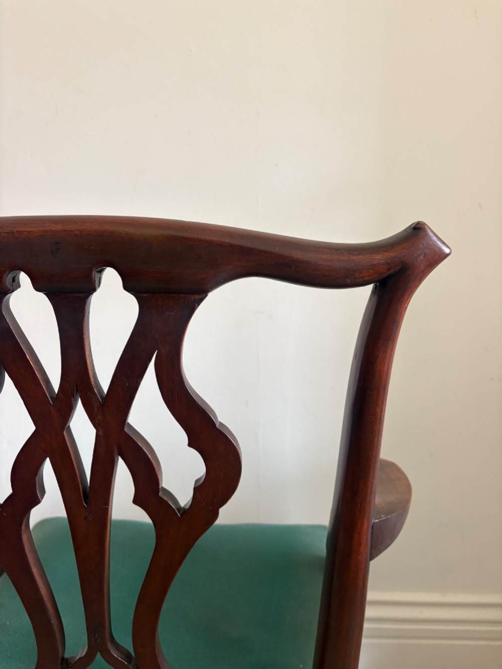 A George III mahogany elbow chair featuring a carved pierced splat back, swept armrests, and a green upholstered seat. View XIV