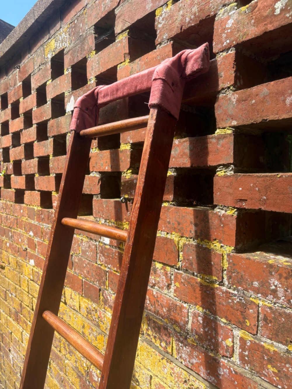 A tall early 20th-century pitch pine and elm library ladder with turned wooden rungs and a padded upper rail leaning against a white wall. View IV