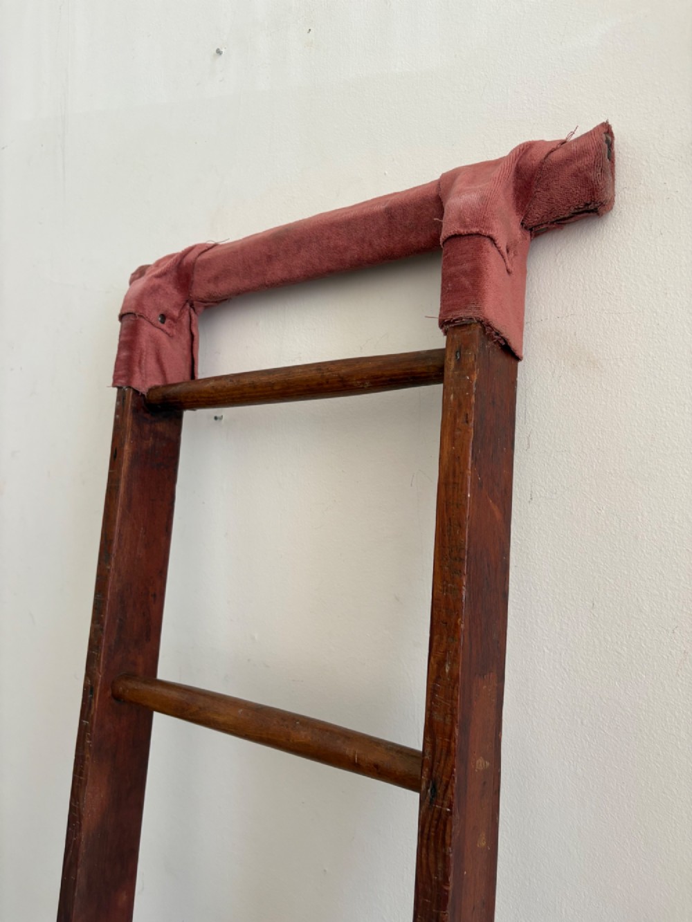 A tall early 20th-century pitch pine and elm library ladder with turned wooden rungs and a padded upper rail leaning against a white wall. View V