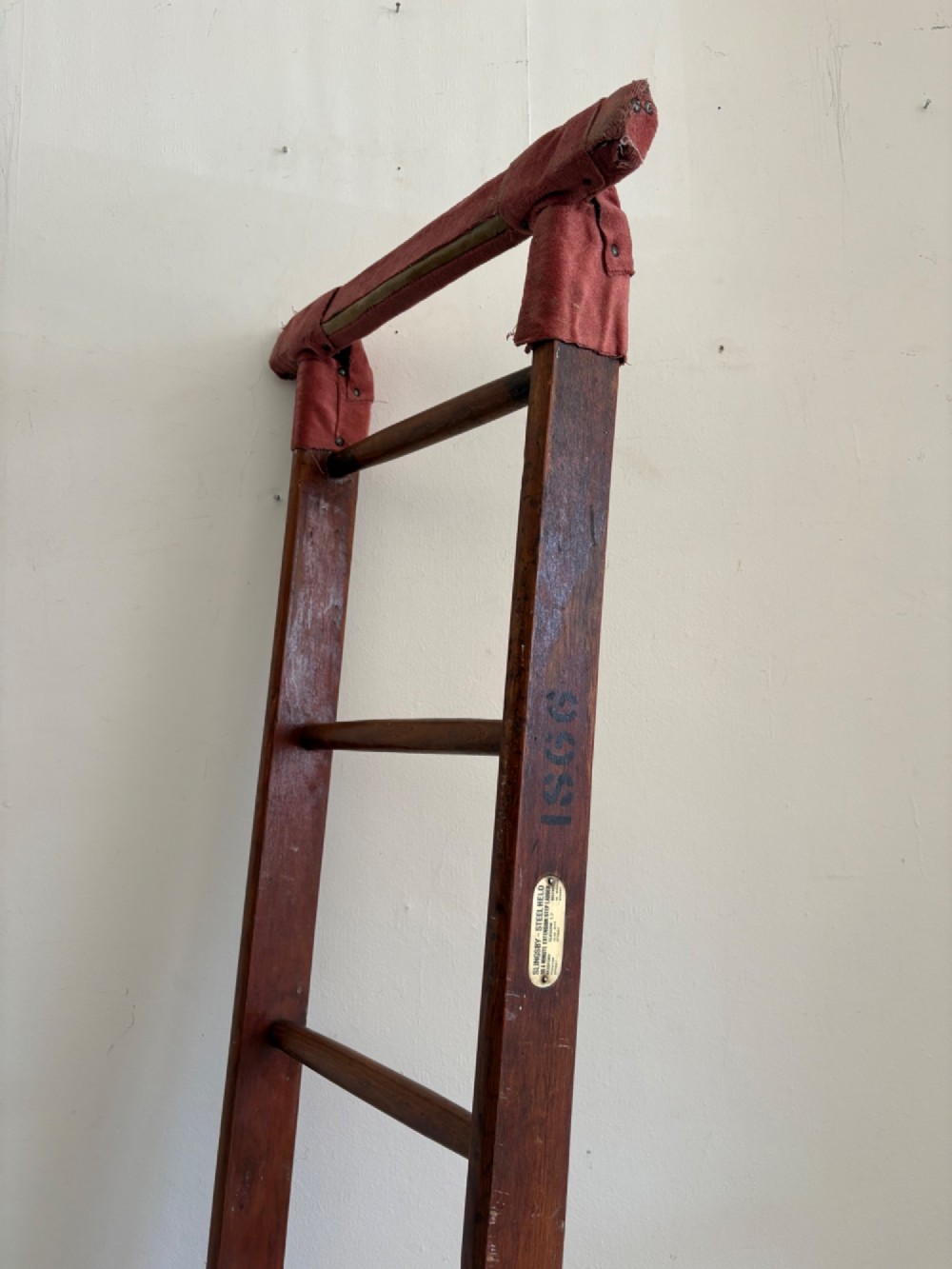 A tall early 20th-century pitch pine and elm library ladder with turned wooden rungs and a padded upper rail leaning against a white wall. View VI