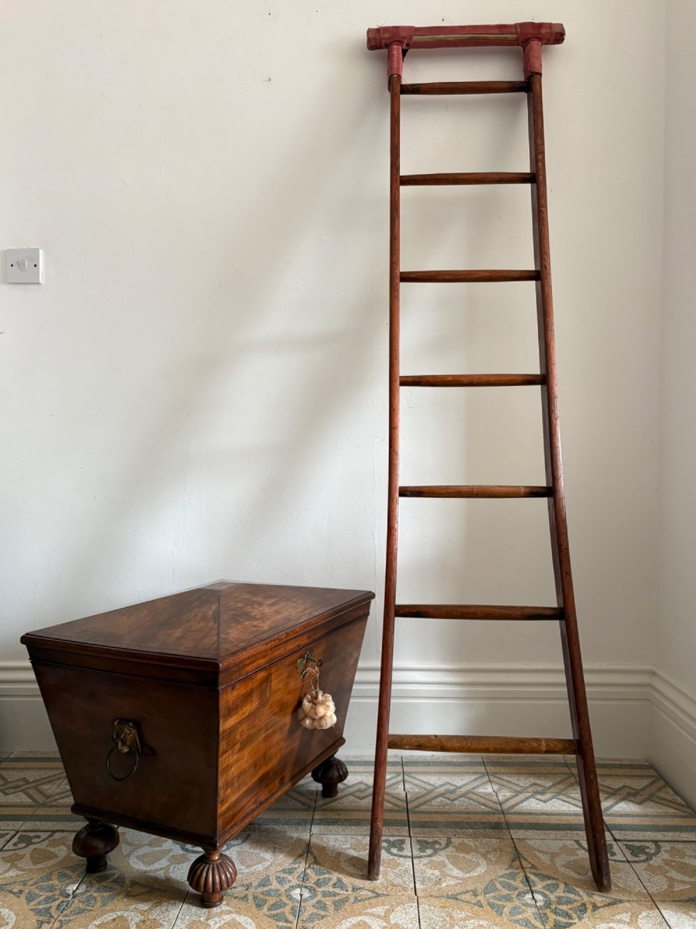 A tall early 20th-century pitch pine and elm library ladder with turned wooden rungs and a padded upper rail leaning against a white wall. View XV