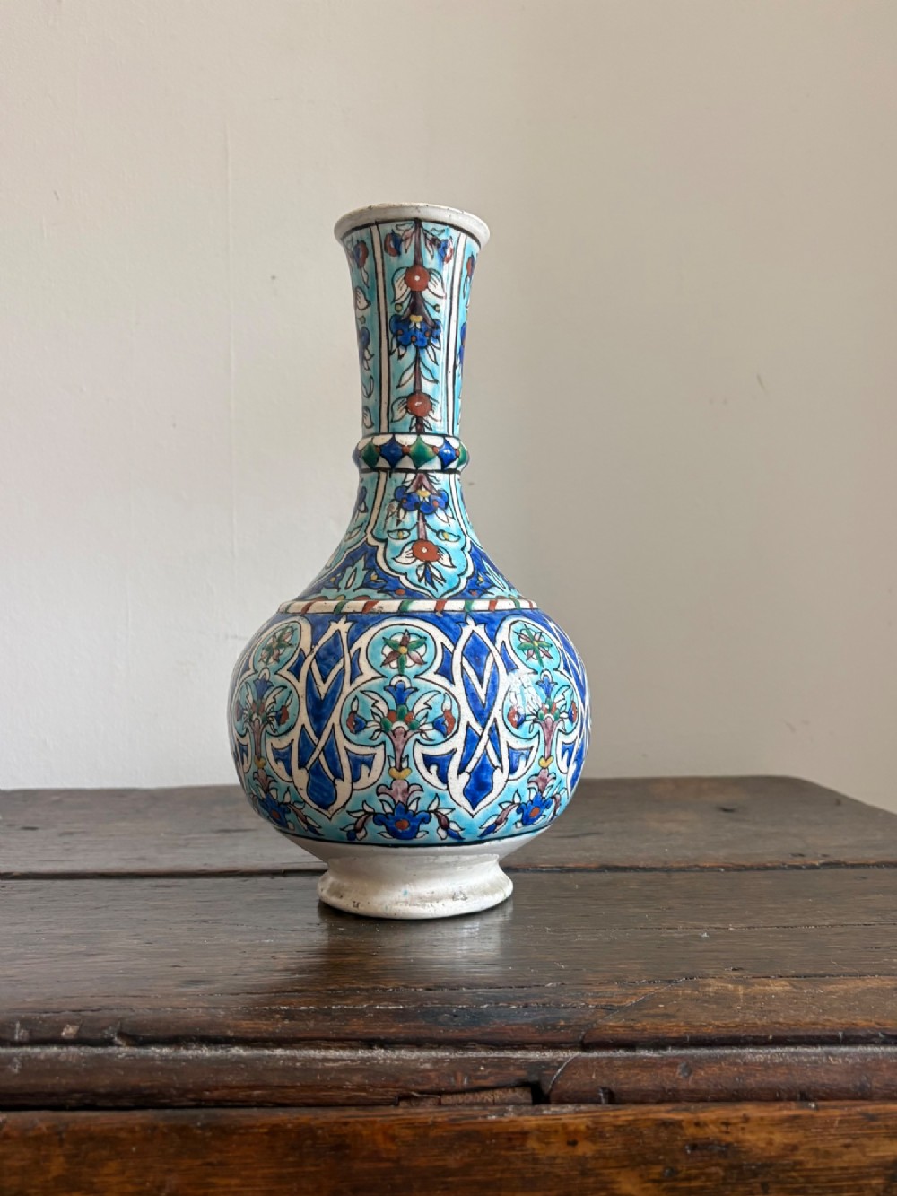 A hand-painted 19th-century Iznik style fritware bottle vase decorated with turquoise, cobalt blue, and red floral arabesque motifs.