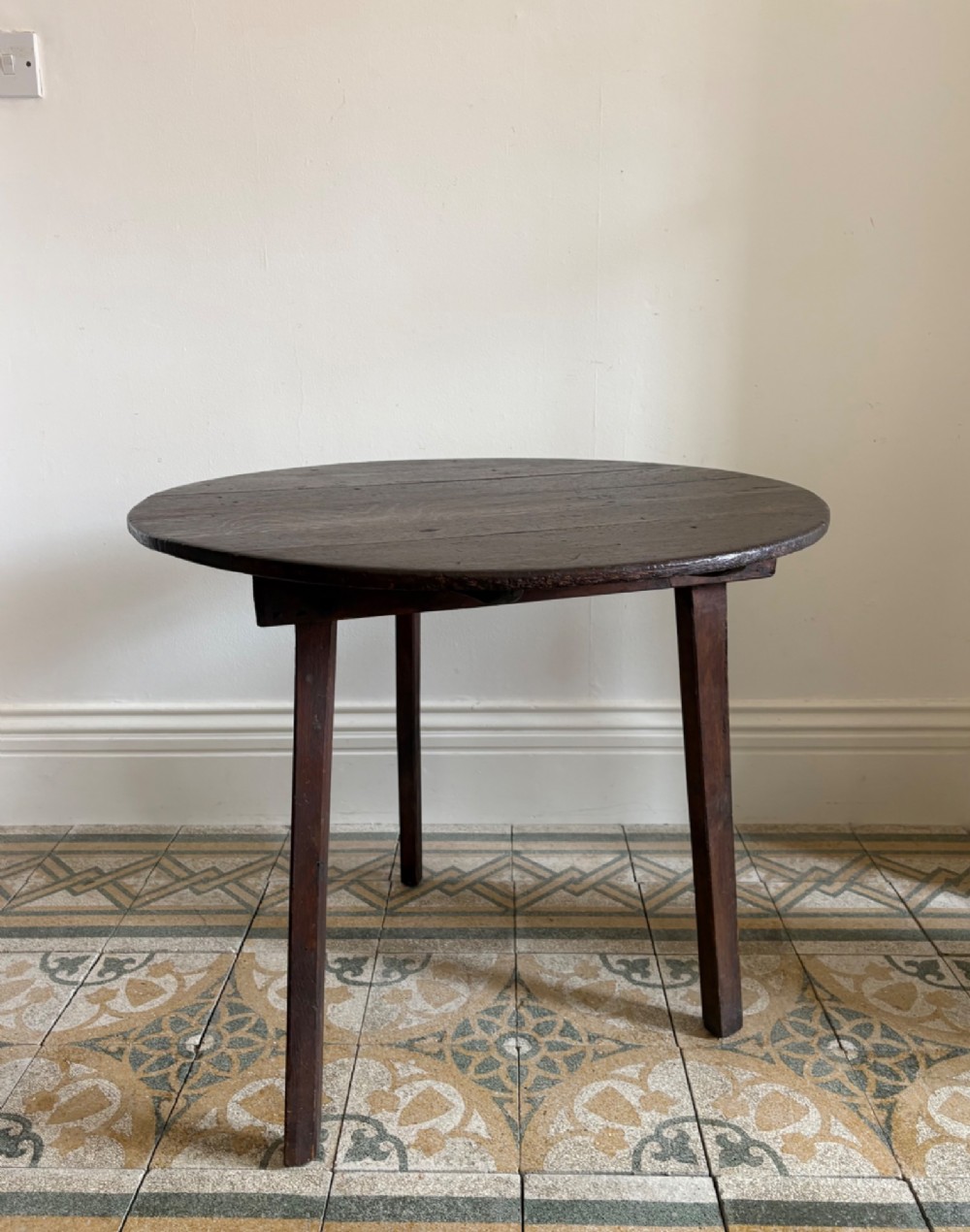 A nineteenth-century round wooden cricket table featuring a circular oak plank top resting on three dark pine legs.